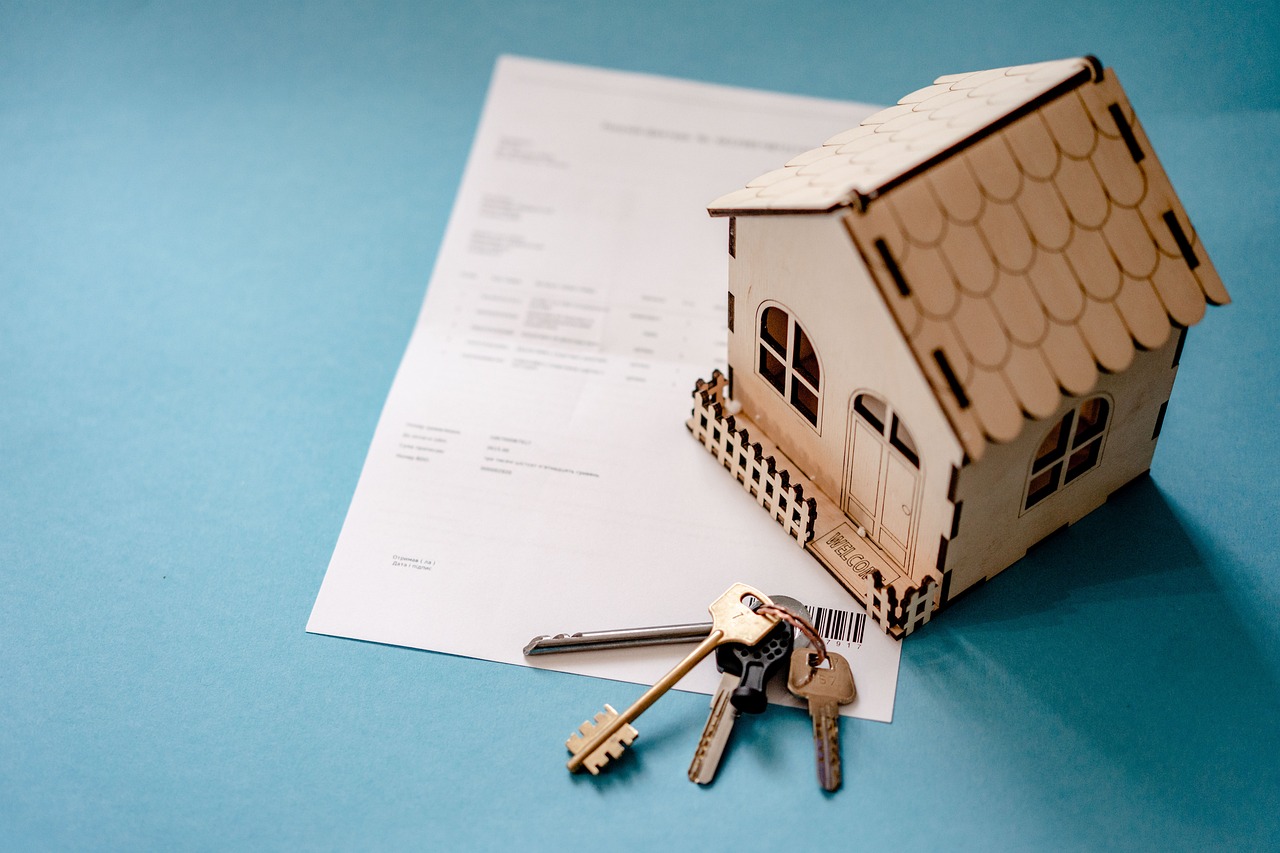 A small wooden house model resting on a contract, with a set of keys beside it