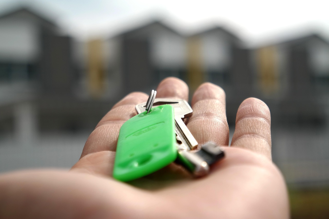 An open hand holding a set of house keys in front of a blurred row of homes